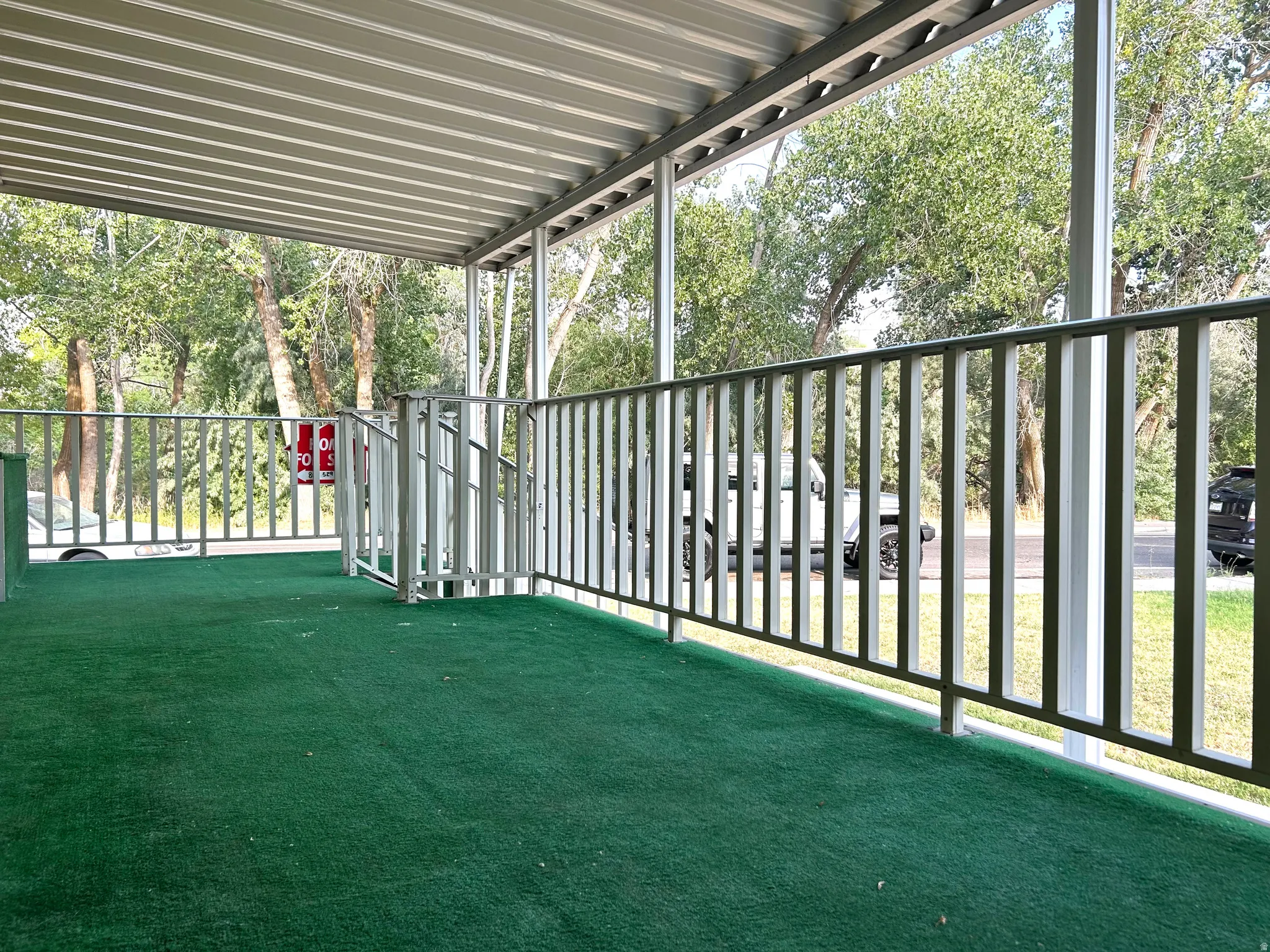 Covered porch featuring a green outdoor carpet, metal railing, and a matching metal roof