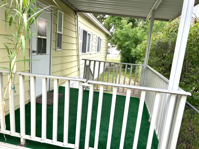 Covered porch featuring white railings, green artificial turf flooring, and a light yellow exterior siding