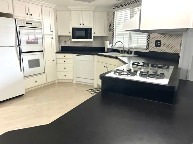 Kitchen featuring light wood-finish flooring, white cabinetry, integrated double oven, and black countertops with an integrated gas cooktop