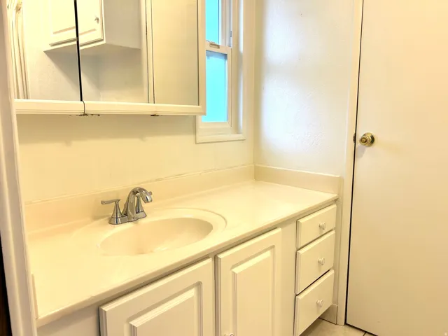 Bathroom vanity featuring an integrated sink, polished chrome faucet, white cabinetry, and a mirrored medicine cabinet