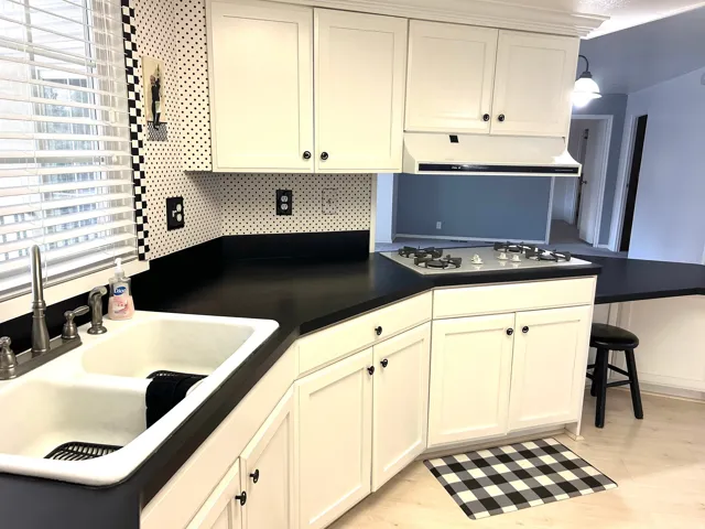 Kitchen featuring white cabinetry with dark hardware, a double basin sink, and a built-in gas range with an overhead vent hood