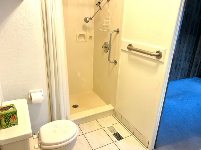 Bathroom featuring light tile,  a standing shower with integrated shelving, and grab bars