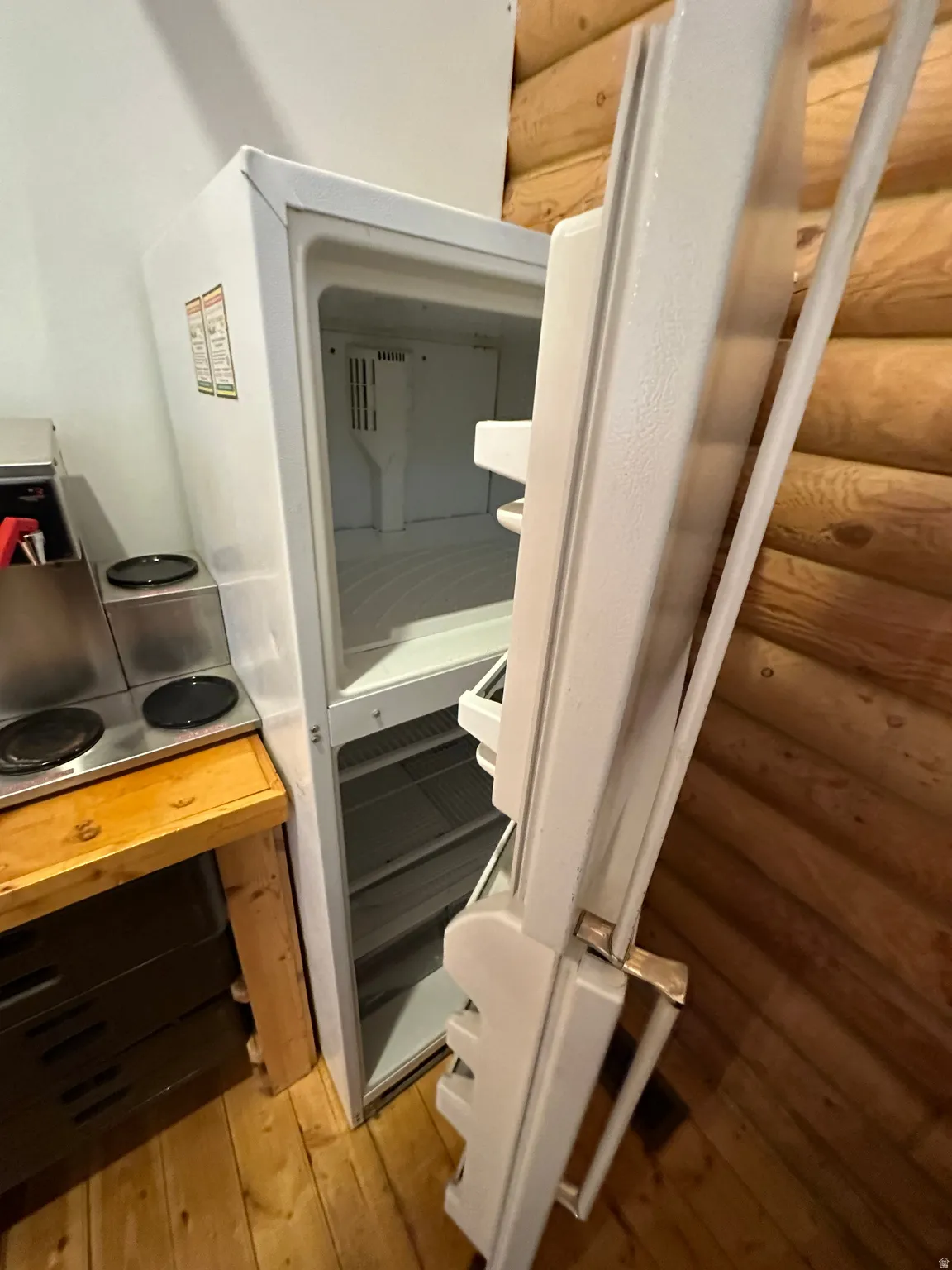 Kitchen view of freestanding refrigerator, light wood-type flooring, and log walls