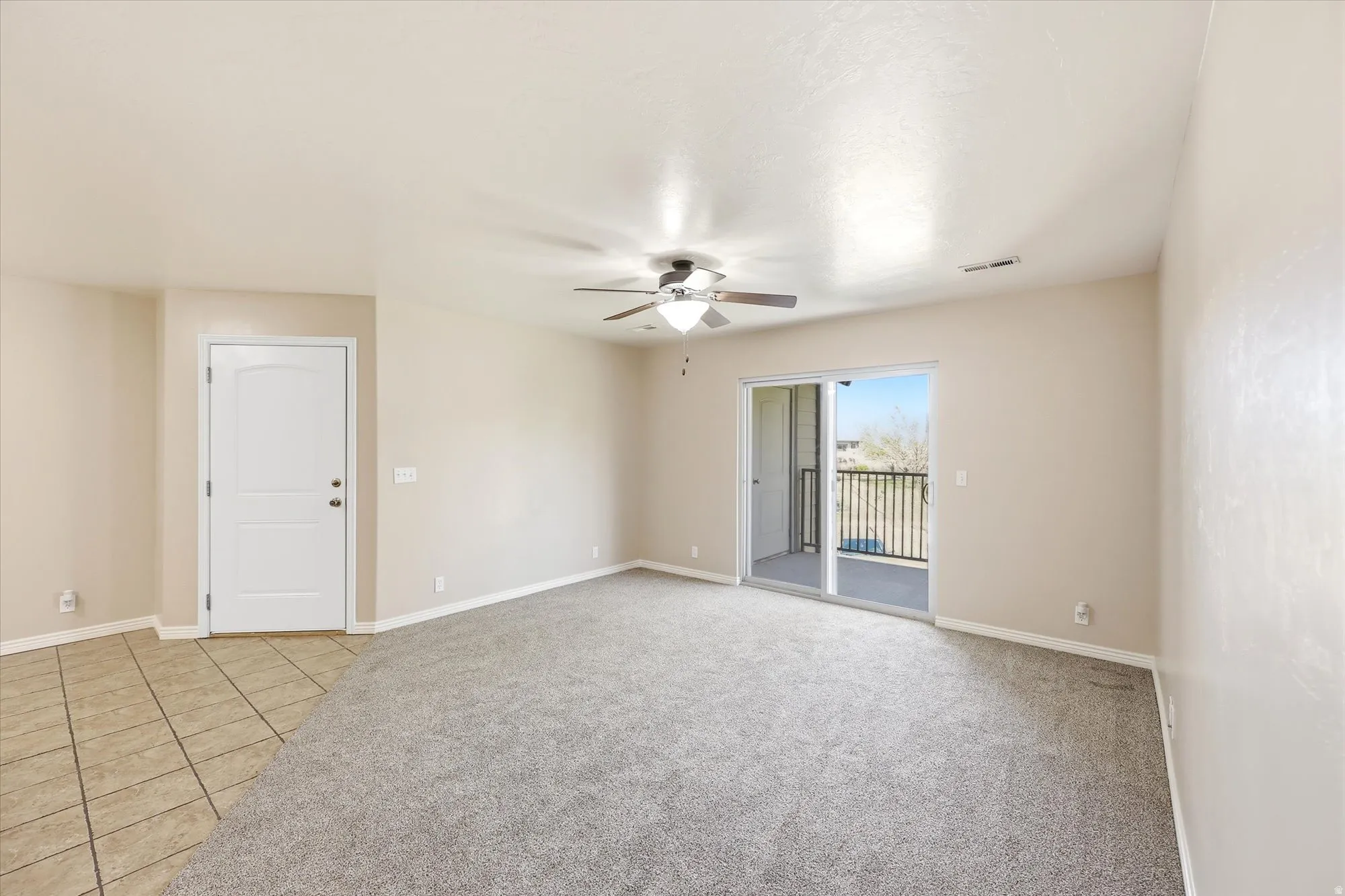 Empty room featuring ceiling fan, light colored carpet, and light tile patterned floors