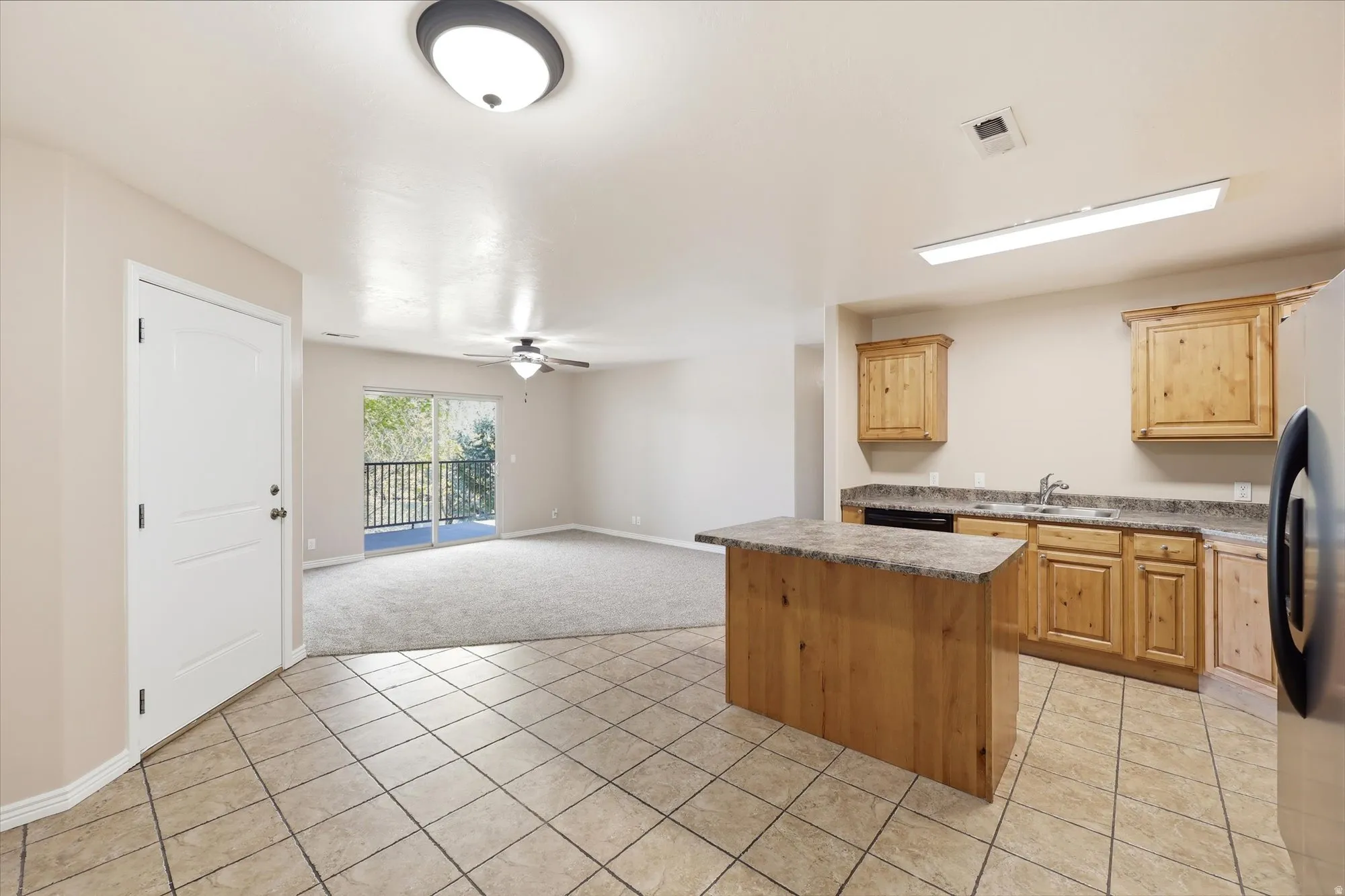 Kitchen with light tile patterned floors, open floor plan, freestanding refrigerator, a ceiling fan, and a kitchen island