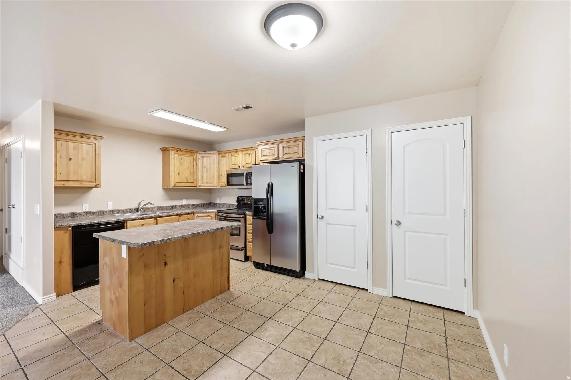 Kitchen with stainless steel appliances, a center island, light wood finish cabinetry, light tile patterned floors, and light countertops