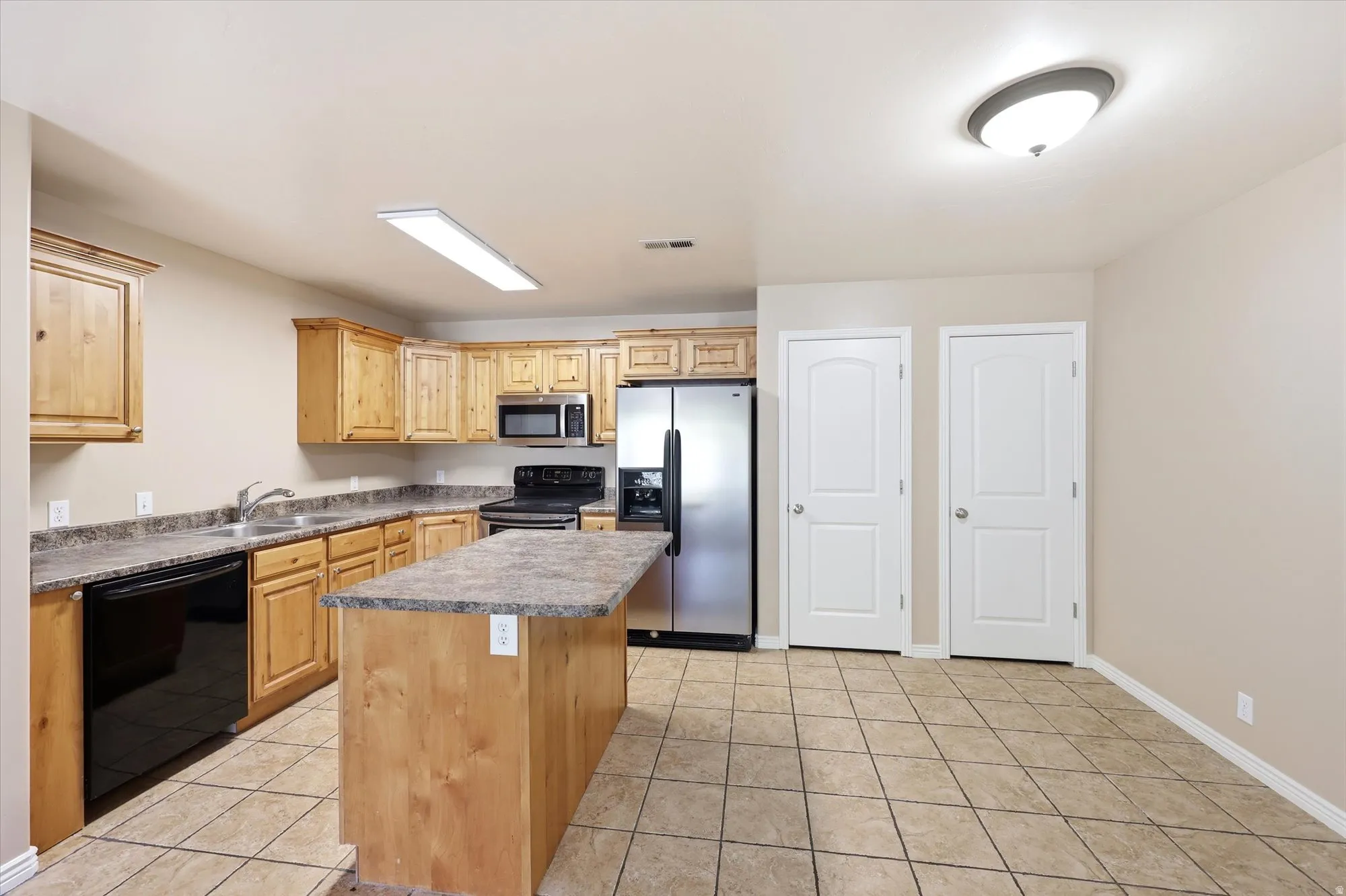 Kitchen featuring black appliances, a kitchen island, light tile patterned flooring, and light wood finish cabinetry