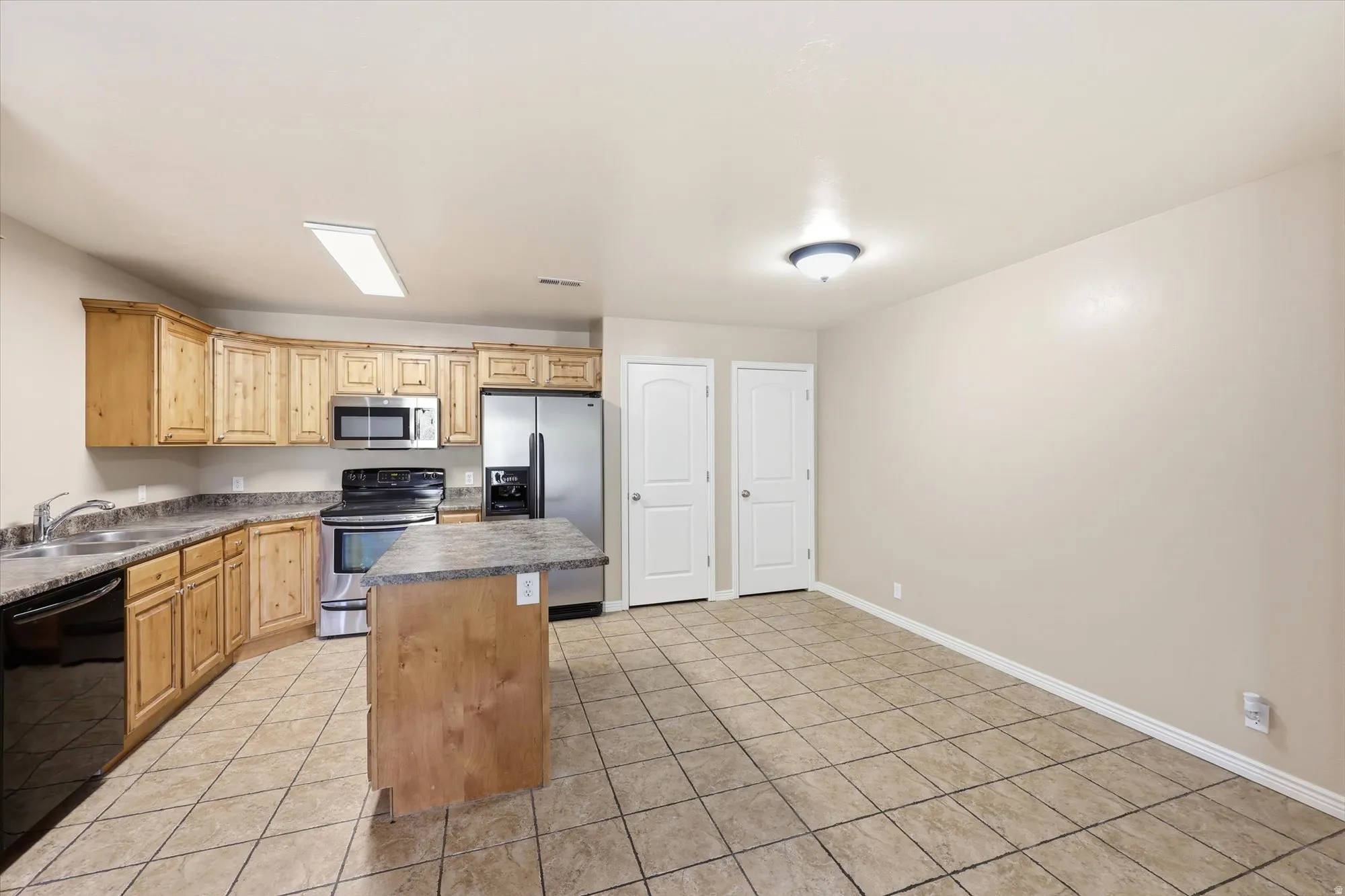 Kitchen with a center island, stainless steel appliances, dark countertops, light tile patterned floors, and light wood finish cabinets
