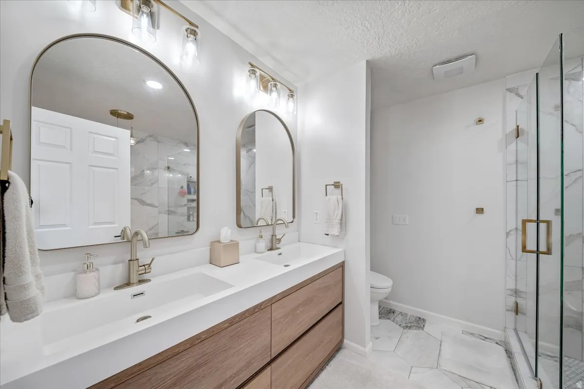Full bath featuring double vanity, light marble finish flooring, a marble finish shower, and a textured ceiling