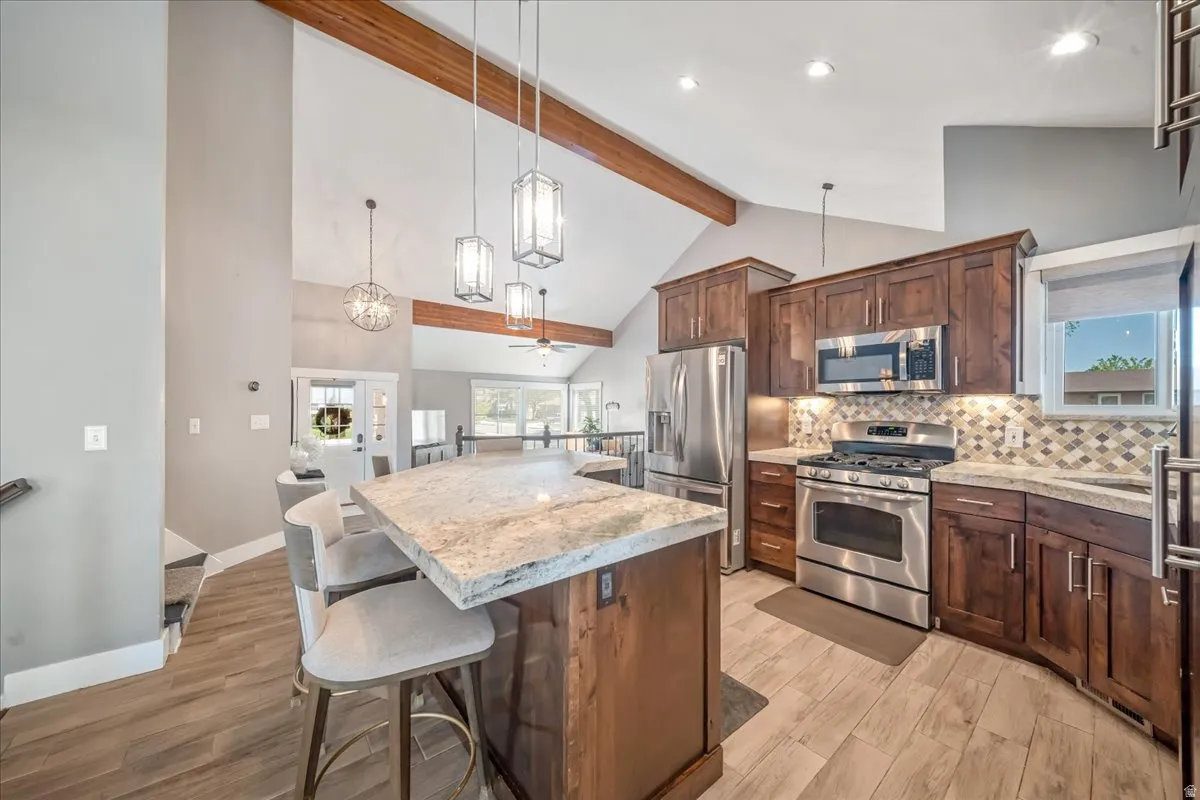 Kitchen with stainless steel appliances, a kitchen island, a breakfast bar area, light wood finished floors, and lofted ceiling