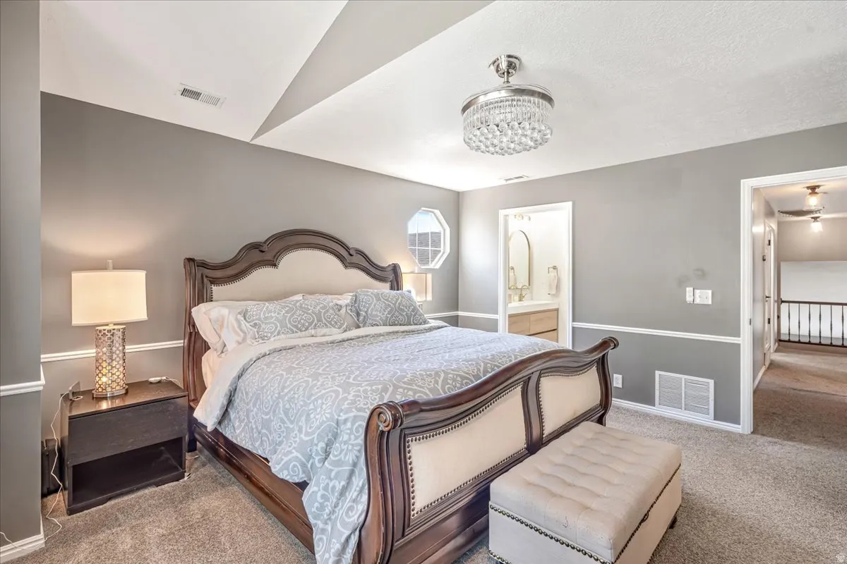 Bedroom featuring light carpet, ensuite bath, and suspended lighting