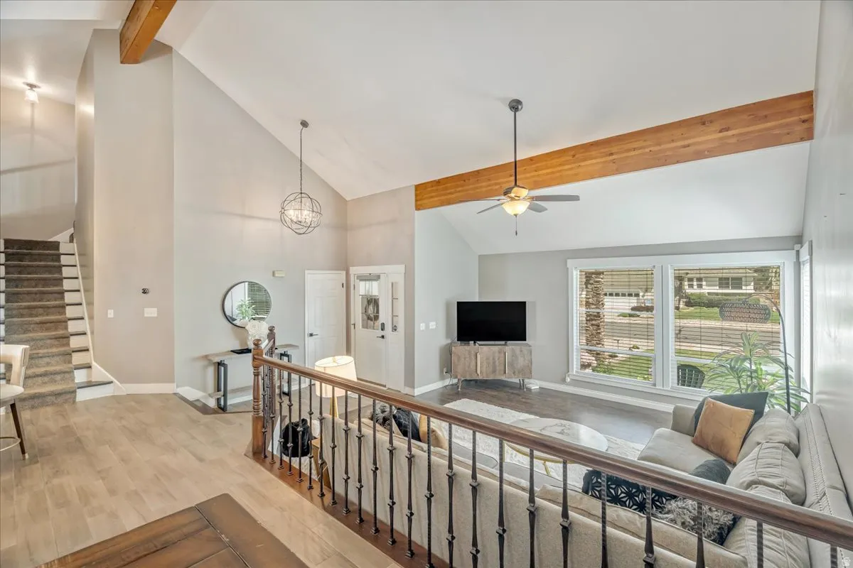 Corridor with light wood-style flooring, vaulted ceiling, suspended lighting, and an upstairs landing