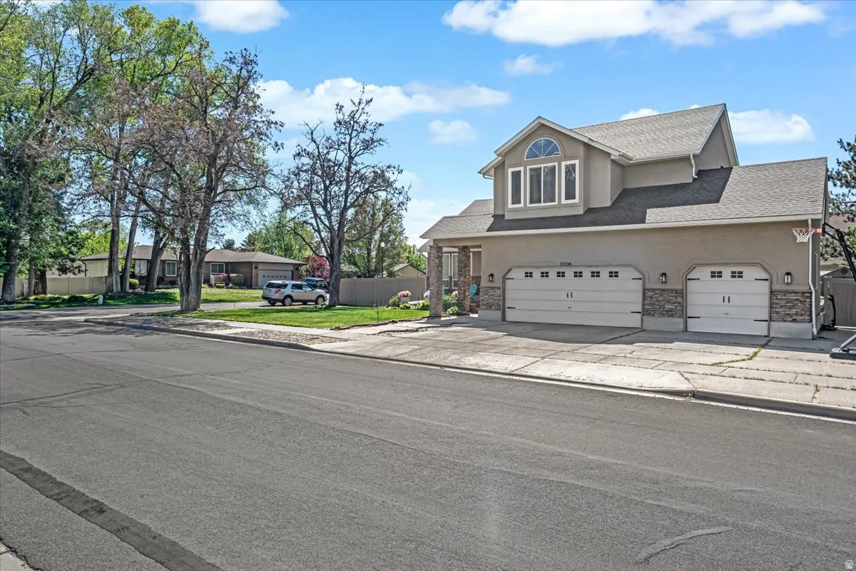 Traditional home with stucco siding, roof with shingles, driveway, stone siding, and a garage