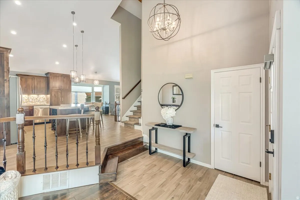 Foyer entrance featuring suspended lighting, light wood-style flooring, and a high ceiling