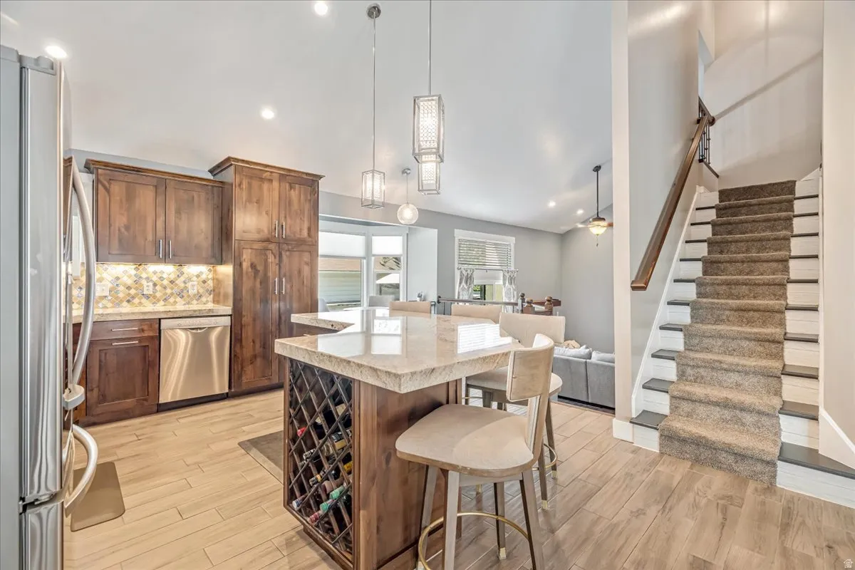 Kitchen featuring stainless steel appliances, a breakfast bar area, light wood-style flooring, a kitchen island, and light stone countertops