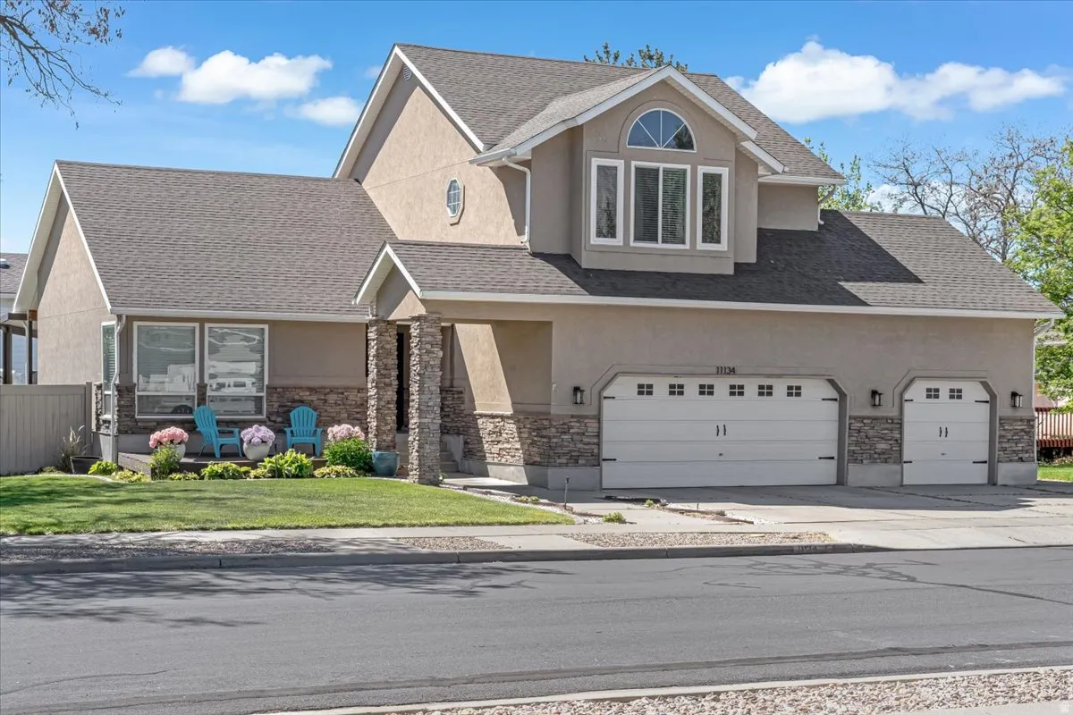 View of front facade featuring stucco siding, concrete driveway, a shingled roof, and stone siding