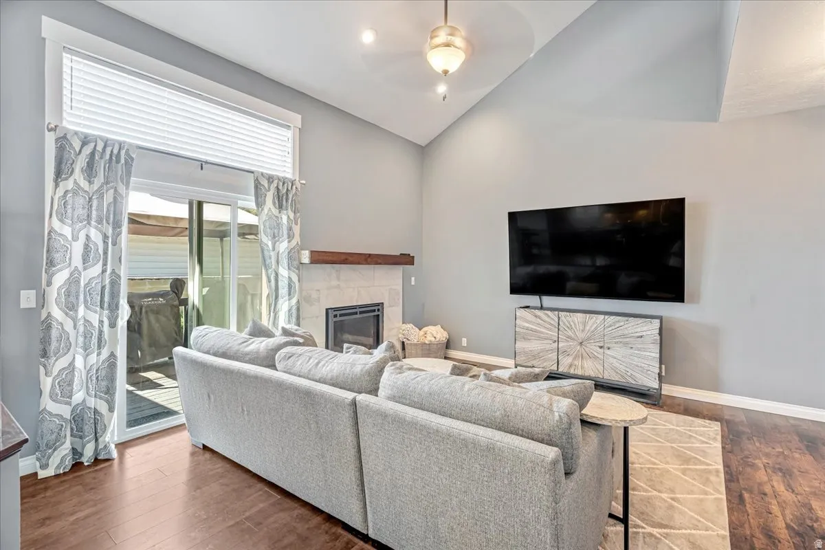 Living area with a ceiling fan, a glass covered fireplace, vaulted ceiling, and dark wood-style floors