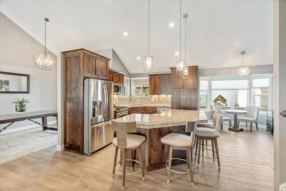 Kitchen with a chandelier, stainless steel appliances, lofted ceiling, light wood finished floors, and a breakfast bar