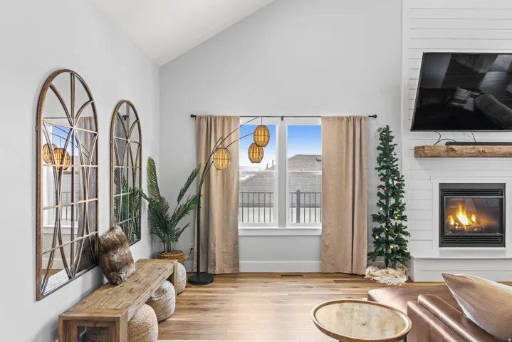 Living area featuring light wood-style floors, vaulted ceiling, and a glass covered fireplace