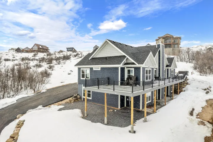Snow covered back of property featuring a deck and roof with shingles