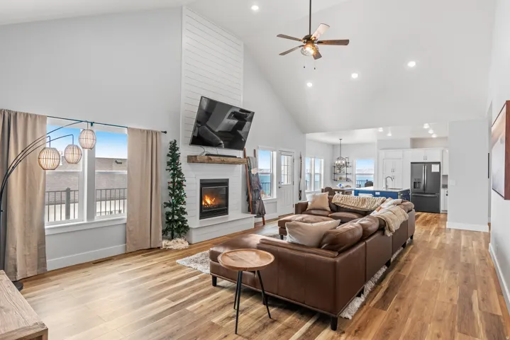 Living area with a ceiling fan, a large fireplace, a chandelier, light wood-style flooring, and vaulted ceiling