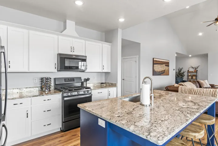 Two tone kitchen featuring stainless steel appliances, open floor plan, light stone countertops, light wood-type flooring, and a kitchen island with sink