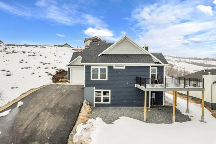 Snow covered house with a garage, a wooden deck, asphalt driveway, and roof with shingles