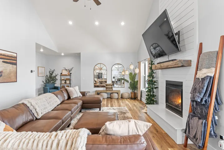 Living room featuring a ceiling fan, light wood-style flooring, a large fireplace, recessed lighting, and lofted ceiling