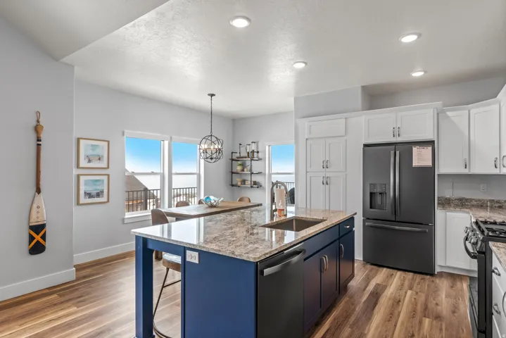 Kitchen featuring stainless steel appliances, two tone cabinets, light stone countertops, light wood-type flooring, and hanging lights