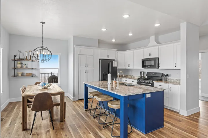 Kitchen with a breakfast bar area, a center island with sink, gas range, refrigerator with ice dispenser, and light stone counters