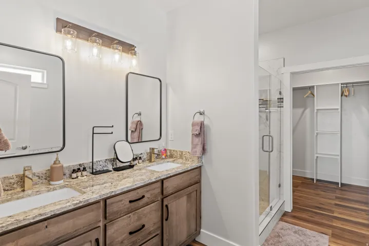 Full bathroom featuring a walk in closet, double vanity, a stall shower, and dark wood finished floors