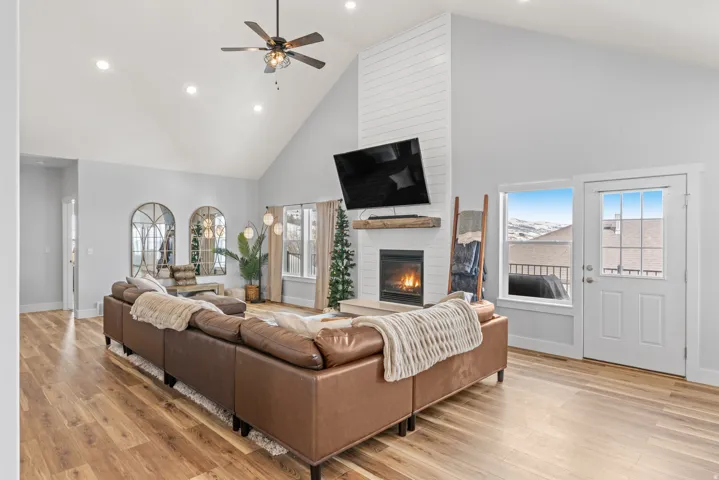 Living room with a high ceiling, a fireplace, light wood-style floors, ceiling fan, and recessed lighting