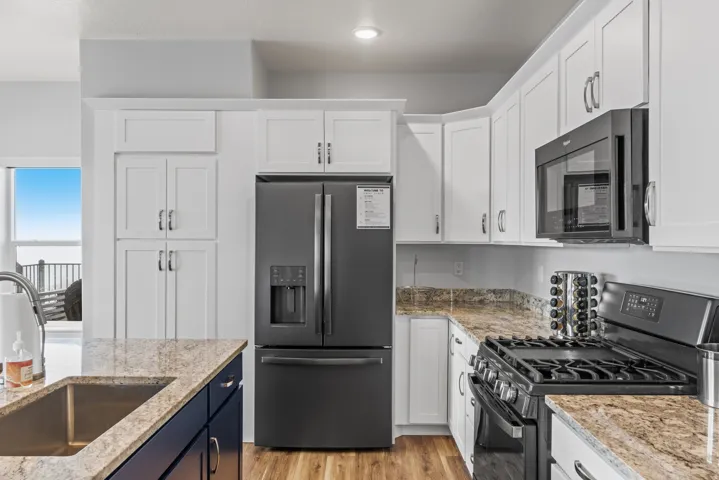 Dual tone kitchen with black appliances, light stone countertops, dual tone cabinets, and light wood-style flooring