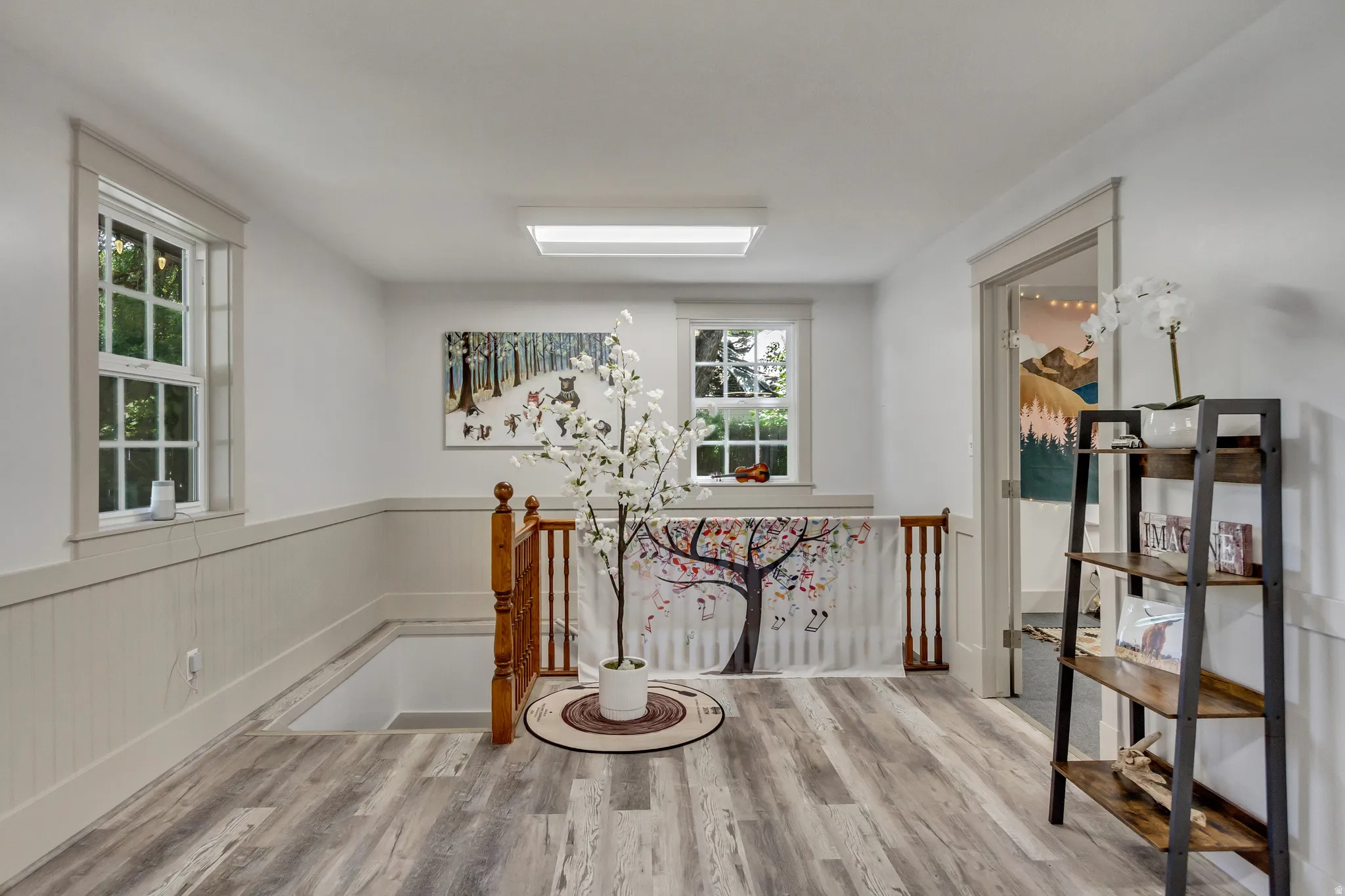 Corridor featuring an upstairs landing, a wainscoted wall, and light wood finished floors