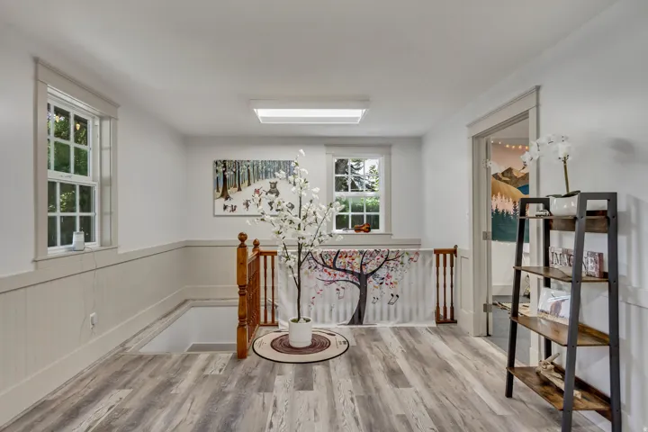 Corridor featuring an upstairs landing, a wainscoted wall, and light wood finished floors