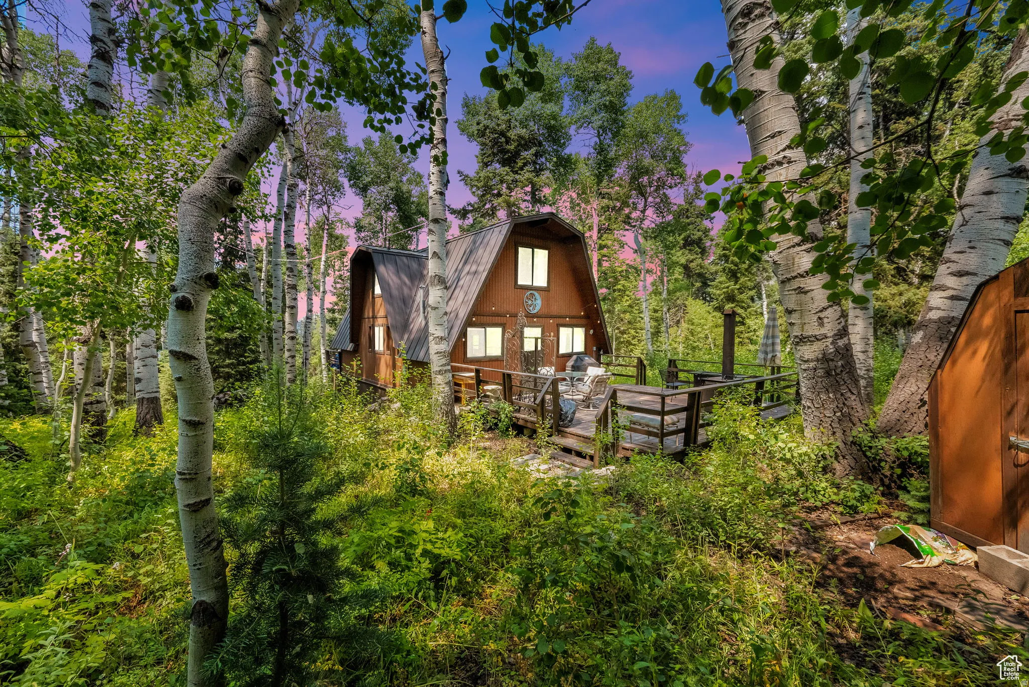 Back of house at dusk featuring a gambrel roof and a deck