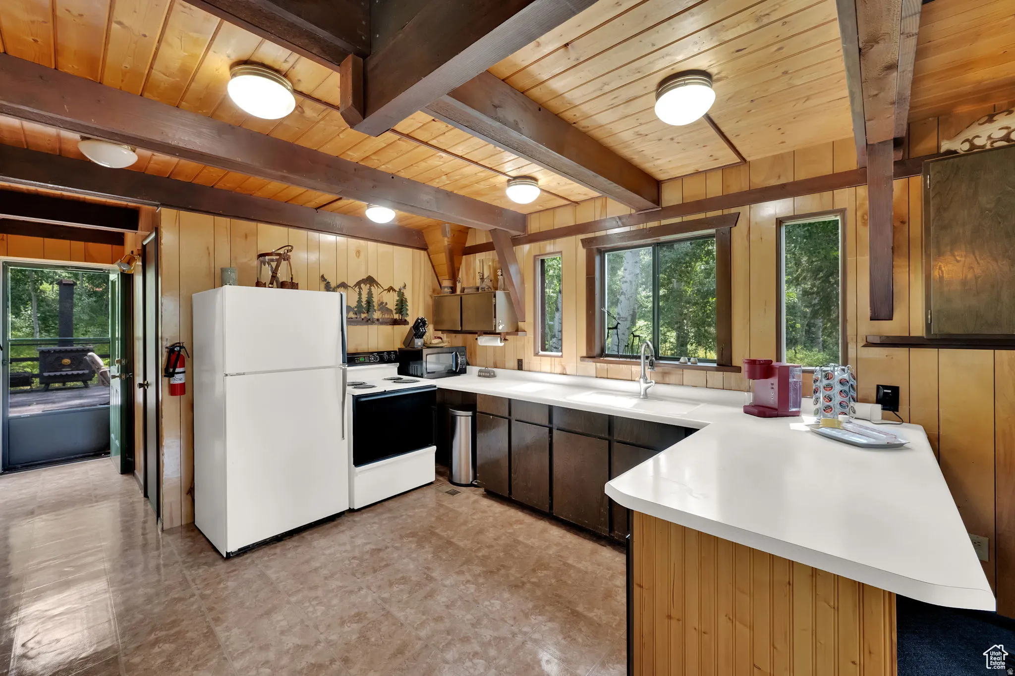 Kitchen with light countertops, white appliances, a peninsula, wooden walls, and healthy amount of natural light