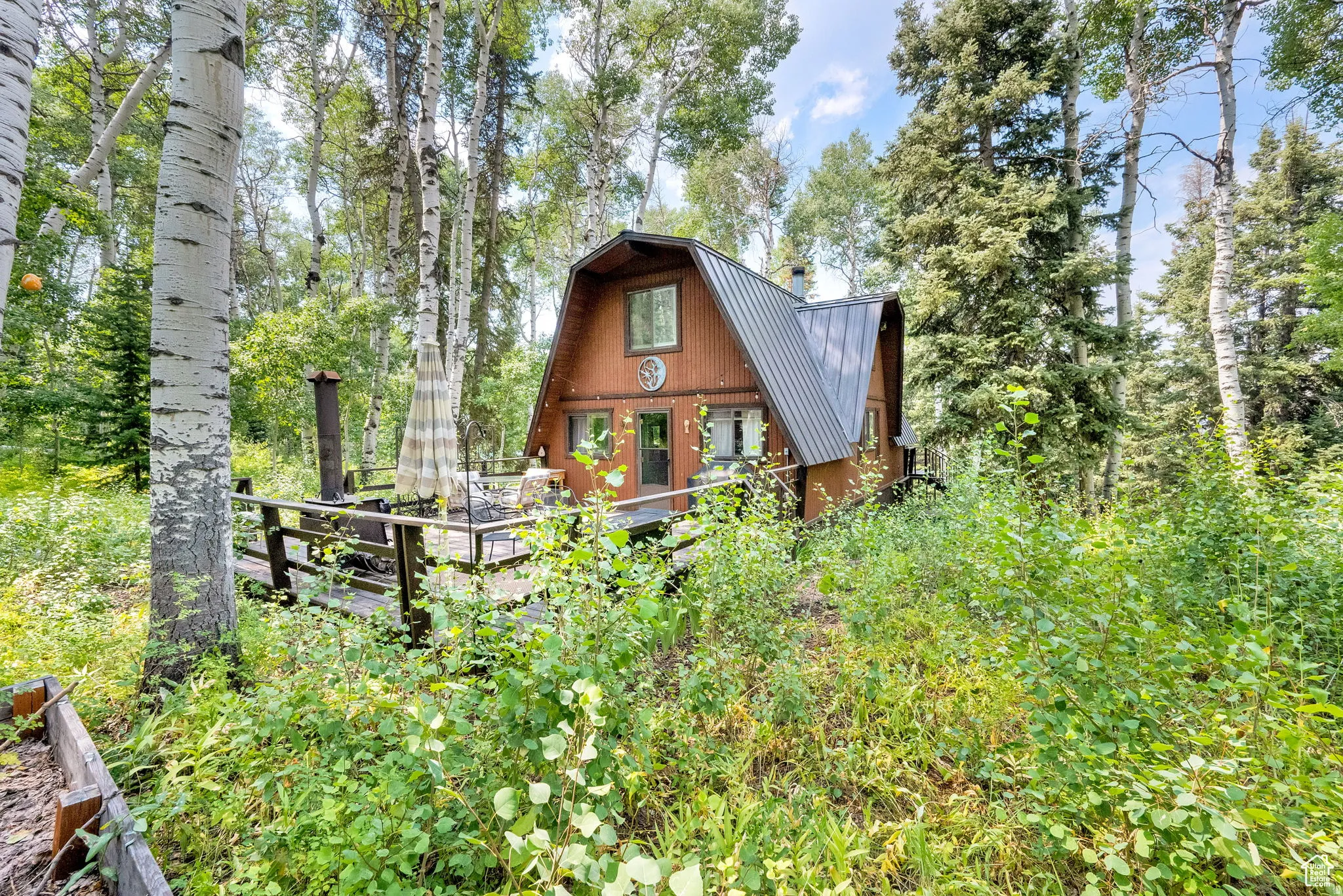 Rear view of house featuring a gambrel roof, a metal roof, and a wooden deck