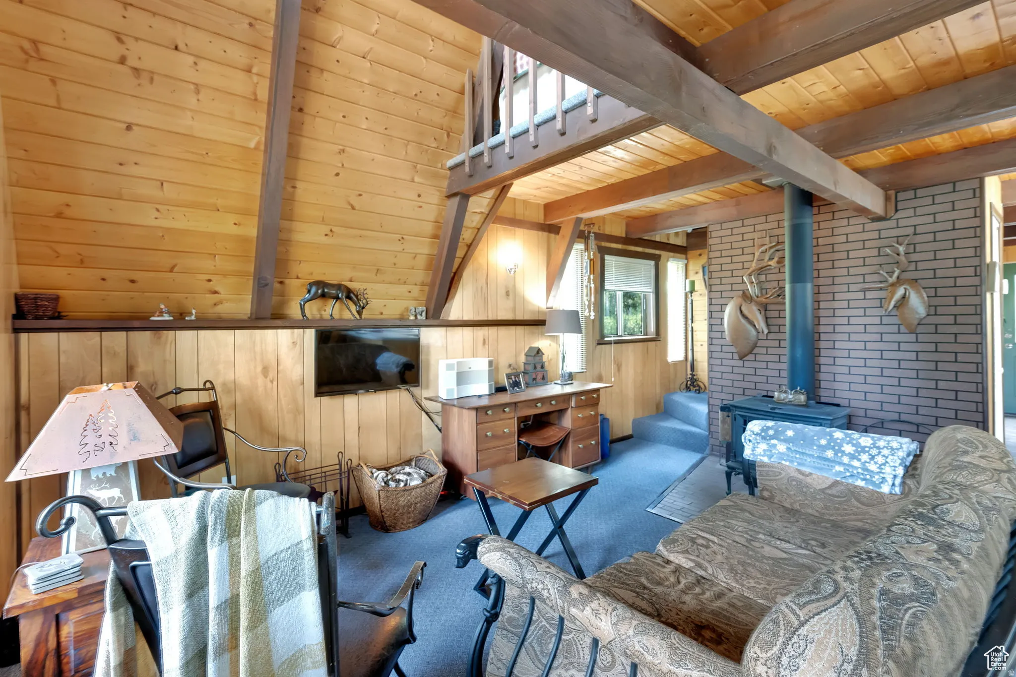Carpeted living area featuring a wood stove, a wood ceiling with exposed beams, brick wall, and wooden walls