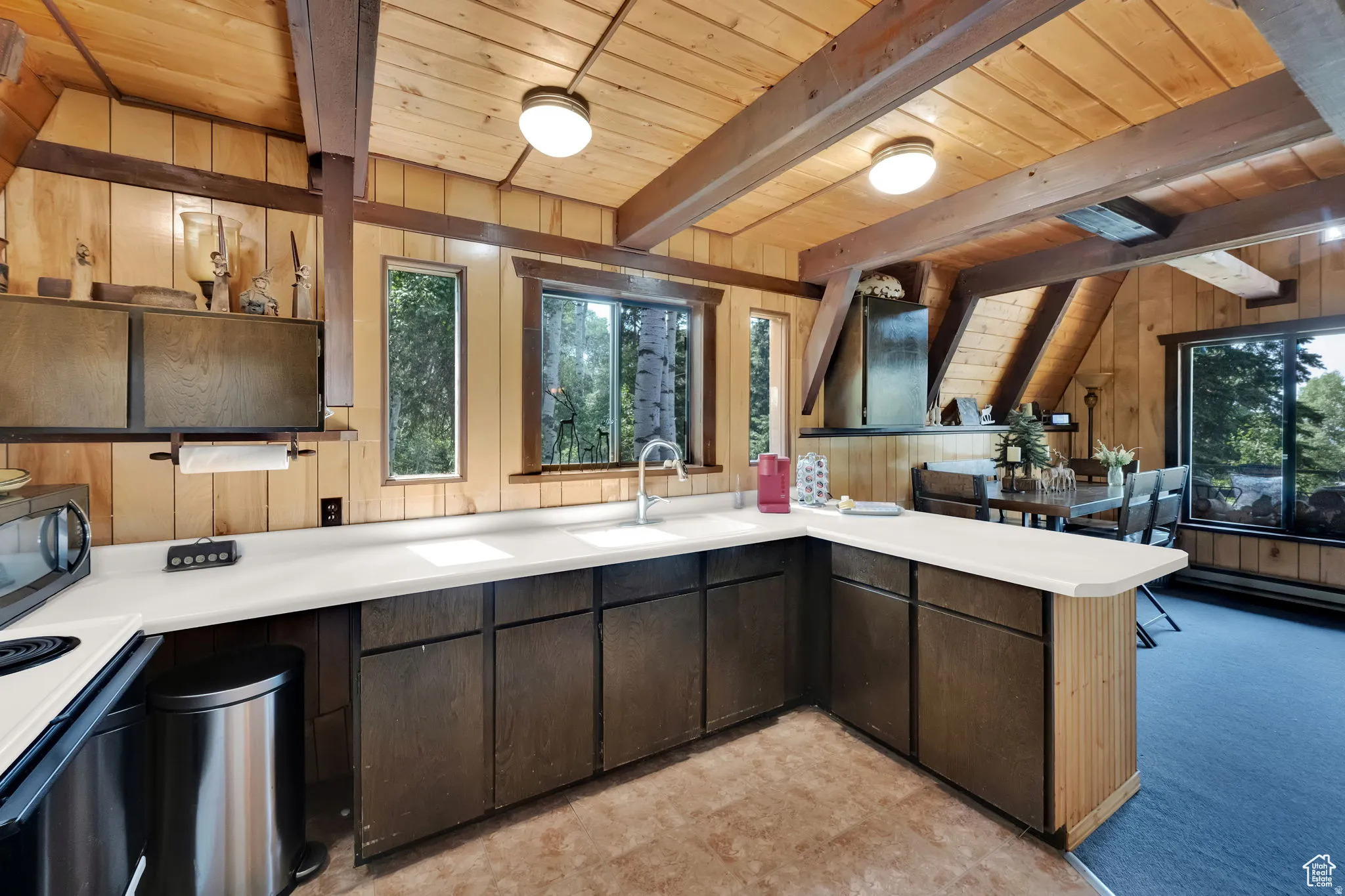 Kitchen with a peninsula, range with electric cooktop, wood walls, a wood ceiling with exposed beams, and healthy amount of natural light