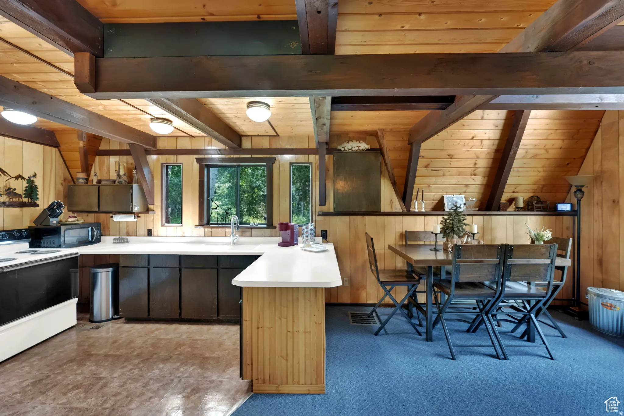 Kitchen featuring white electric range oven, a peninsula, a wood ceiling with exposed beams, light countertops, and light colored carpet