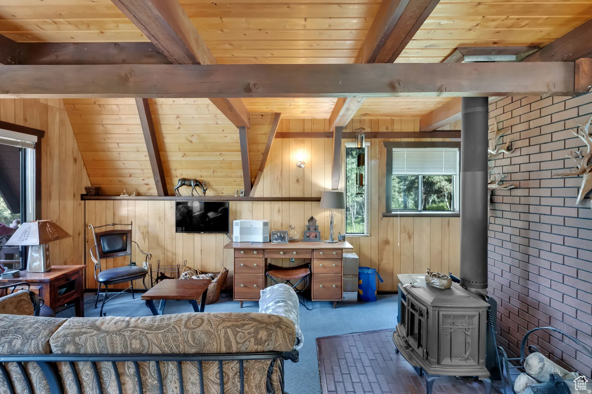 Living area with a wood ceiling with exposed beams, a wood stove, wood walls, and carpet flooring
