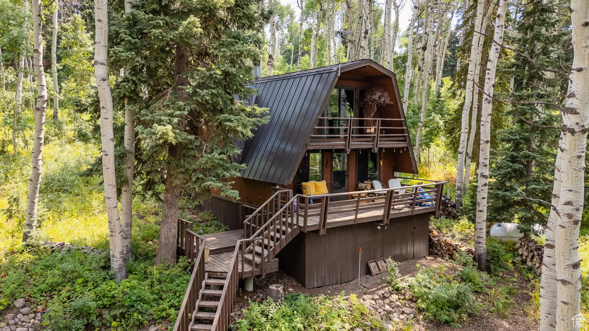 Rear view of property featuring a gambrel roof, a metal roof, a wooden deck, a balcony, and a forest view