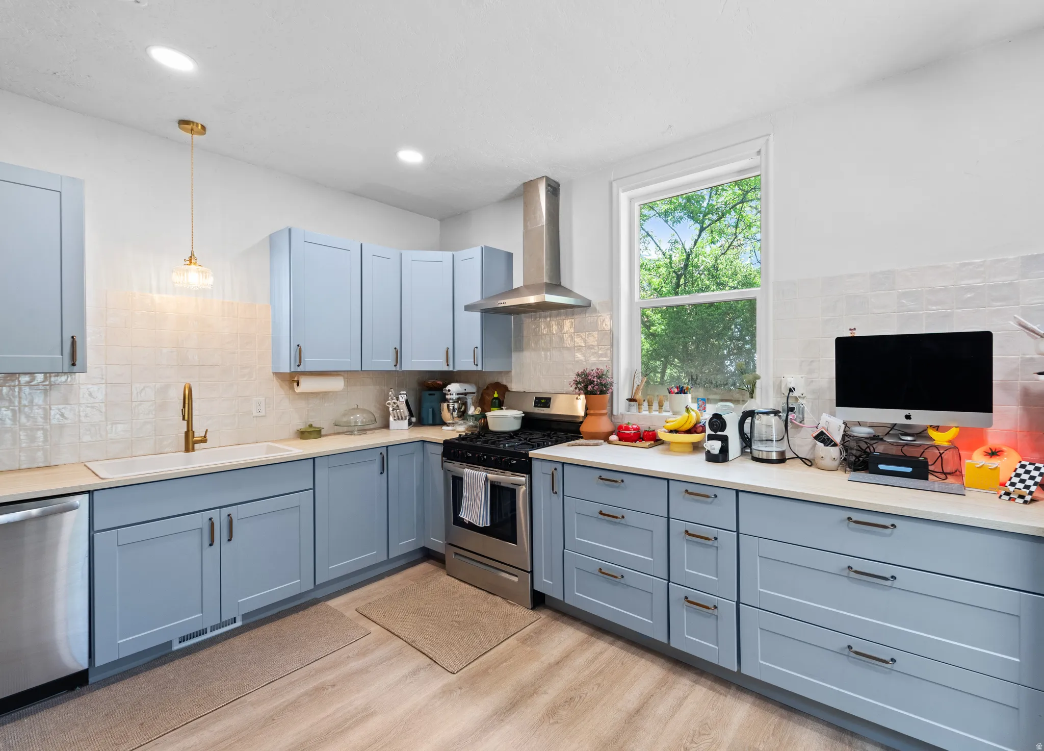 Kitchen with stainless steel appliances, light wood-style floors, decorative light fixtures, and backsplash