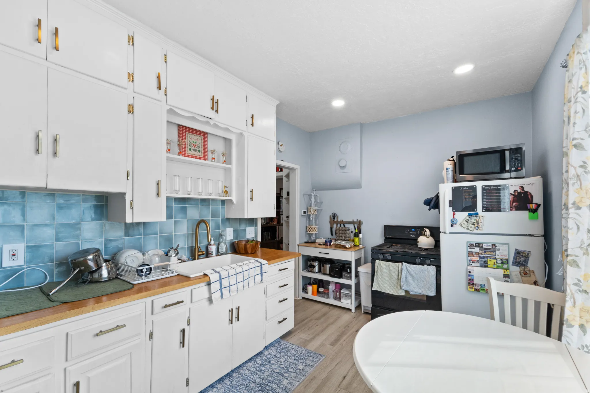 Kitchen with freestanding refrigerator, white cabinetry, open shelves, tasteful backsplash, and black gas stove