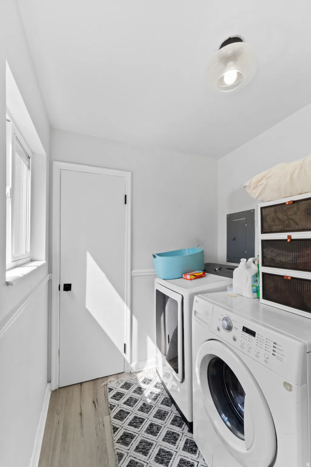 Laundry area with independent washer and dryer, electric panel, and light wood-type flooring