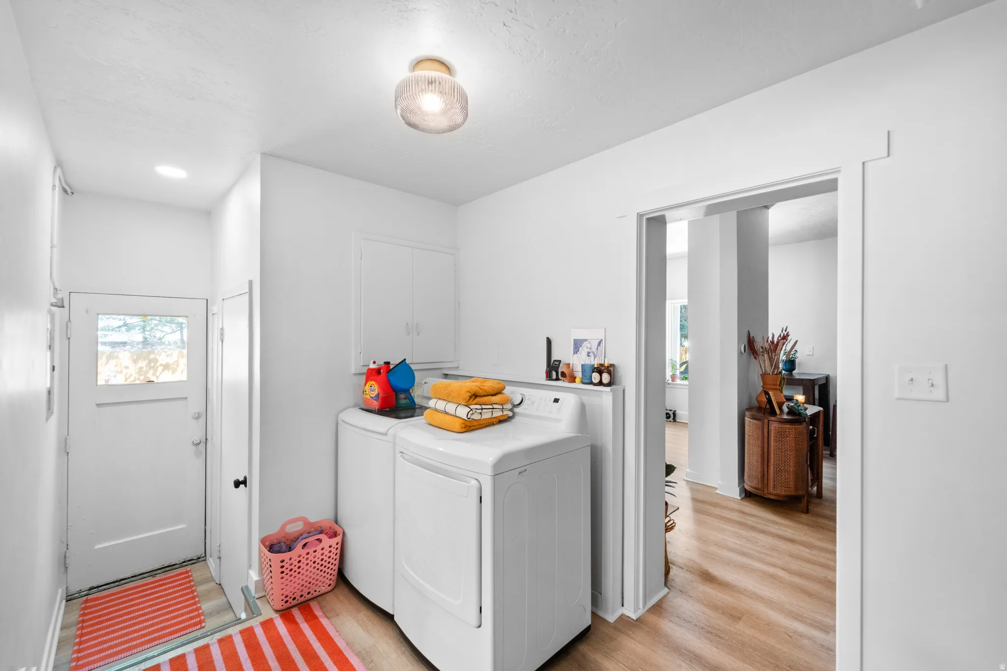 Laundry room with separate washer and dryer, light wood-type flooring, cabinet space, and a textured ceiling