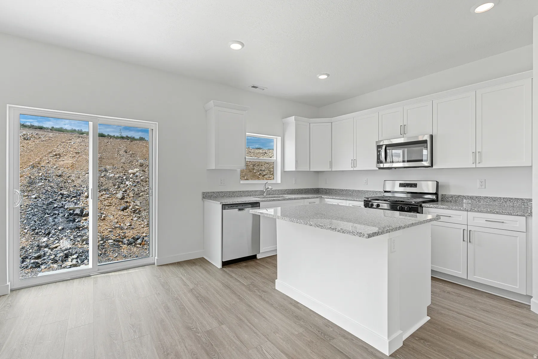 Kitchen with white cabinetry, light stone counters, stainless steel appliances, light wood finished floors, and a kitchen island