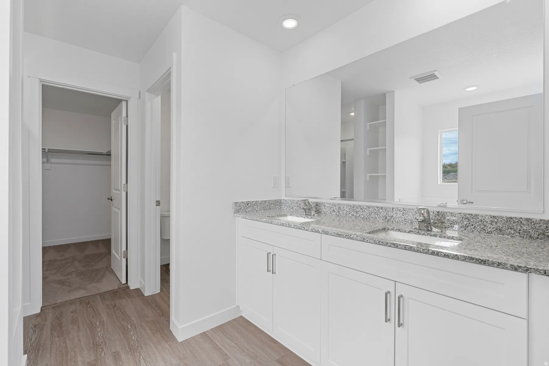 Bathroom featuring double vanity, a spacious closet, light wood-style flooring, and recessed lighting