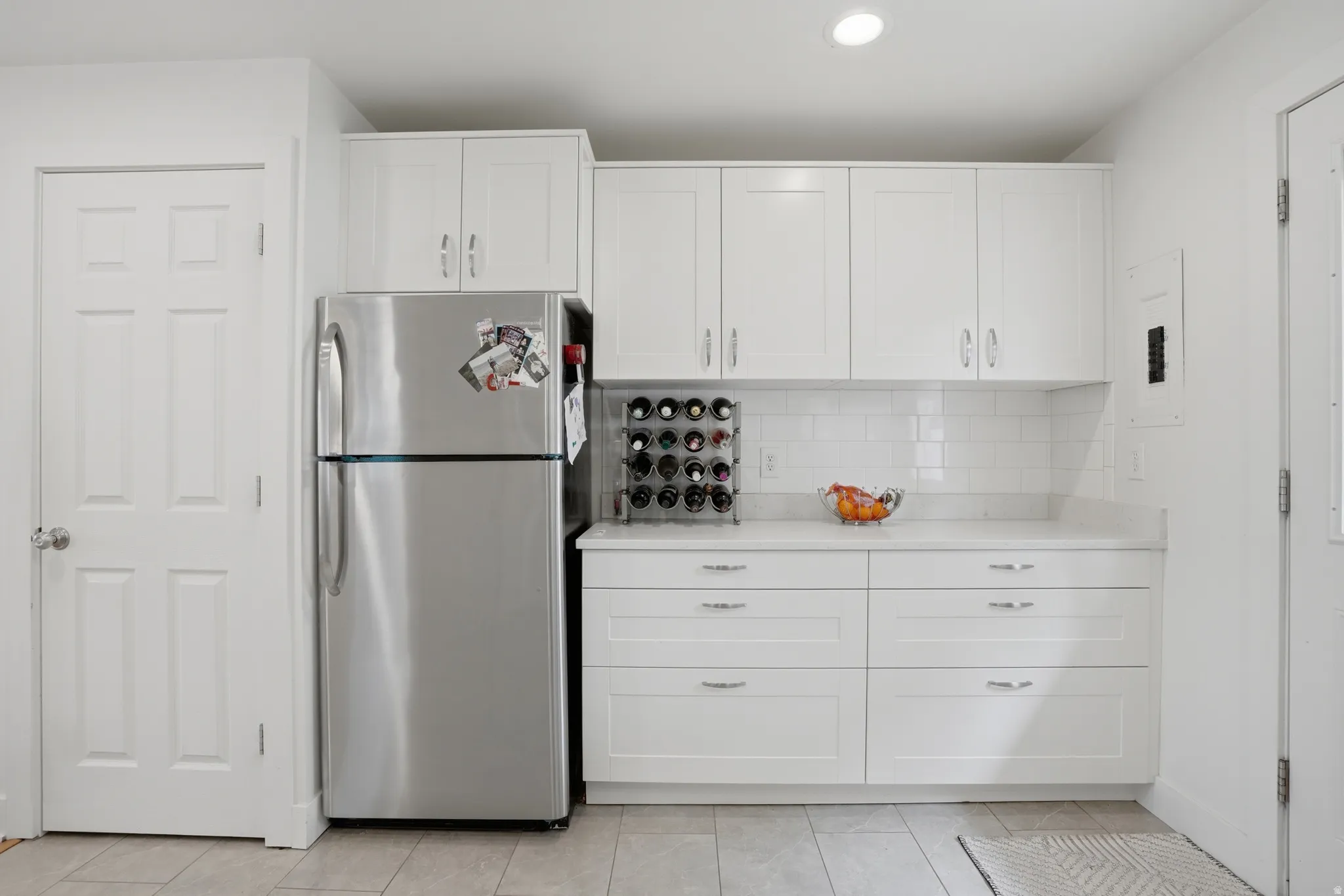 Kitchen featuring freestanding refrigerator, white cabinets, decorative backsplash, recessed lighting, and electric panel